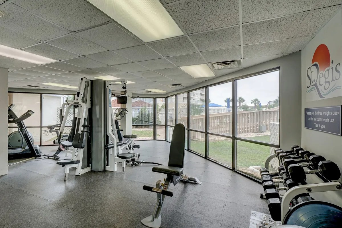 A bright and airy fitness center featuring exercise equipment, a weight rack, and large windows that let in natural light. The space encourages wellness breaks with energizing views and a motivational atmosphere.