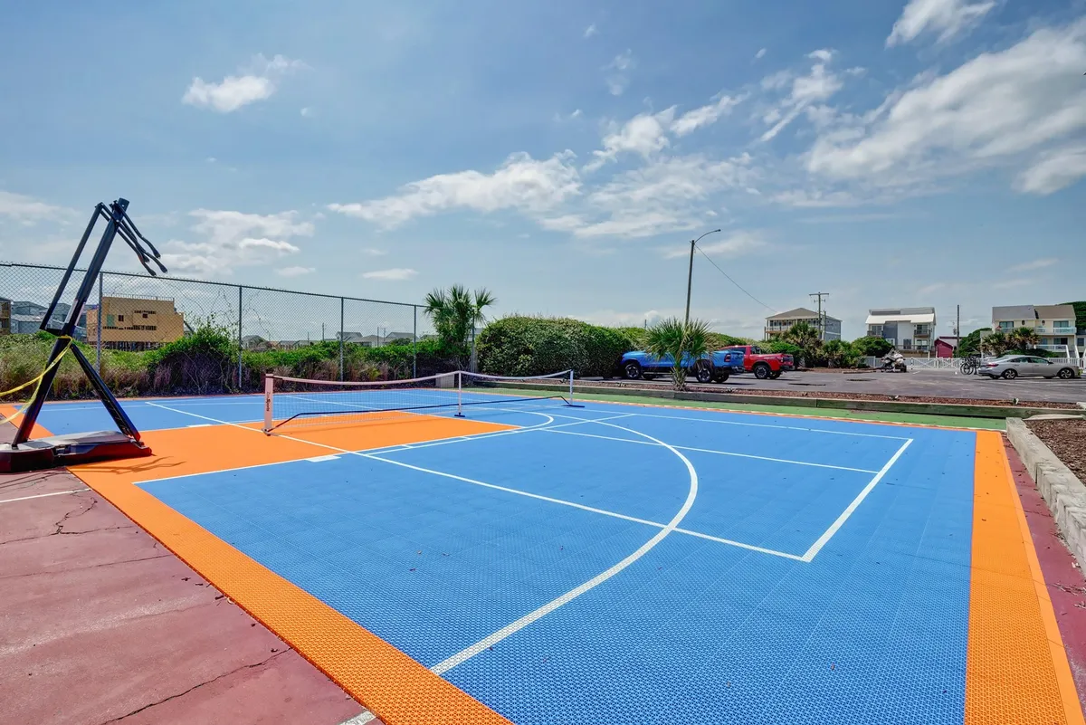 This exterior image captures a vibrant recreation area with a basketball court, tennis net, and colorful flooring, all surrounded by lush greenery. The space appears ready for friendly competitions and group play, embodying the energetic, communal atmosphere described in the section.