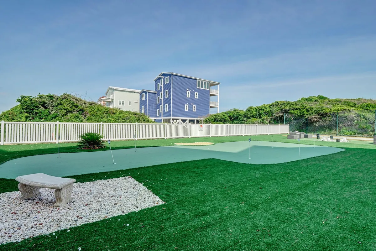 A manicured artificial putting green with landscaped greenery and an inviting outdoor seating area. The scene suggests leisurely afternoons spent enjoying golf practice or casual gatherings with friends against a backdrop of natural beauty.
