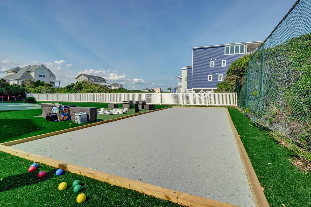 An inviting bocce ball court is set on a manicured green lawn, with colorful bocce balls scattered and nearby homes in view. The scene suggests playful gatherings and relaxed outdoor enjoyment, ideal for multi-generational families and friend groups.