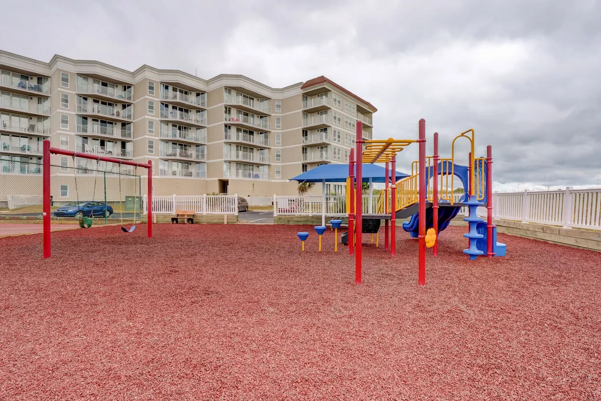 A bright, modern playground with swings and sturdy red rubber ground cover, bustling with children at play. The scene radiates joy and a sense of safety, with families nearby engaging in conversation and supervision.